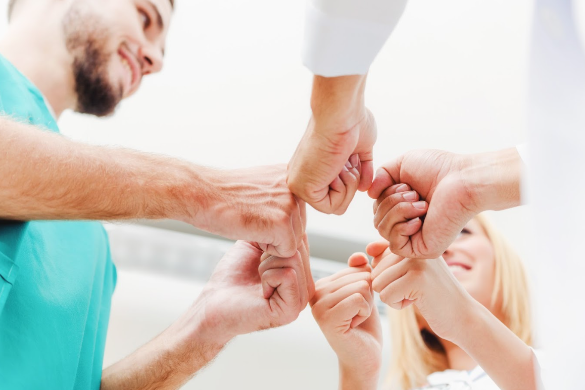 Drei Pflegekräfte machen einen Team-Bump um sich zu motivieren